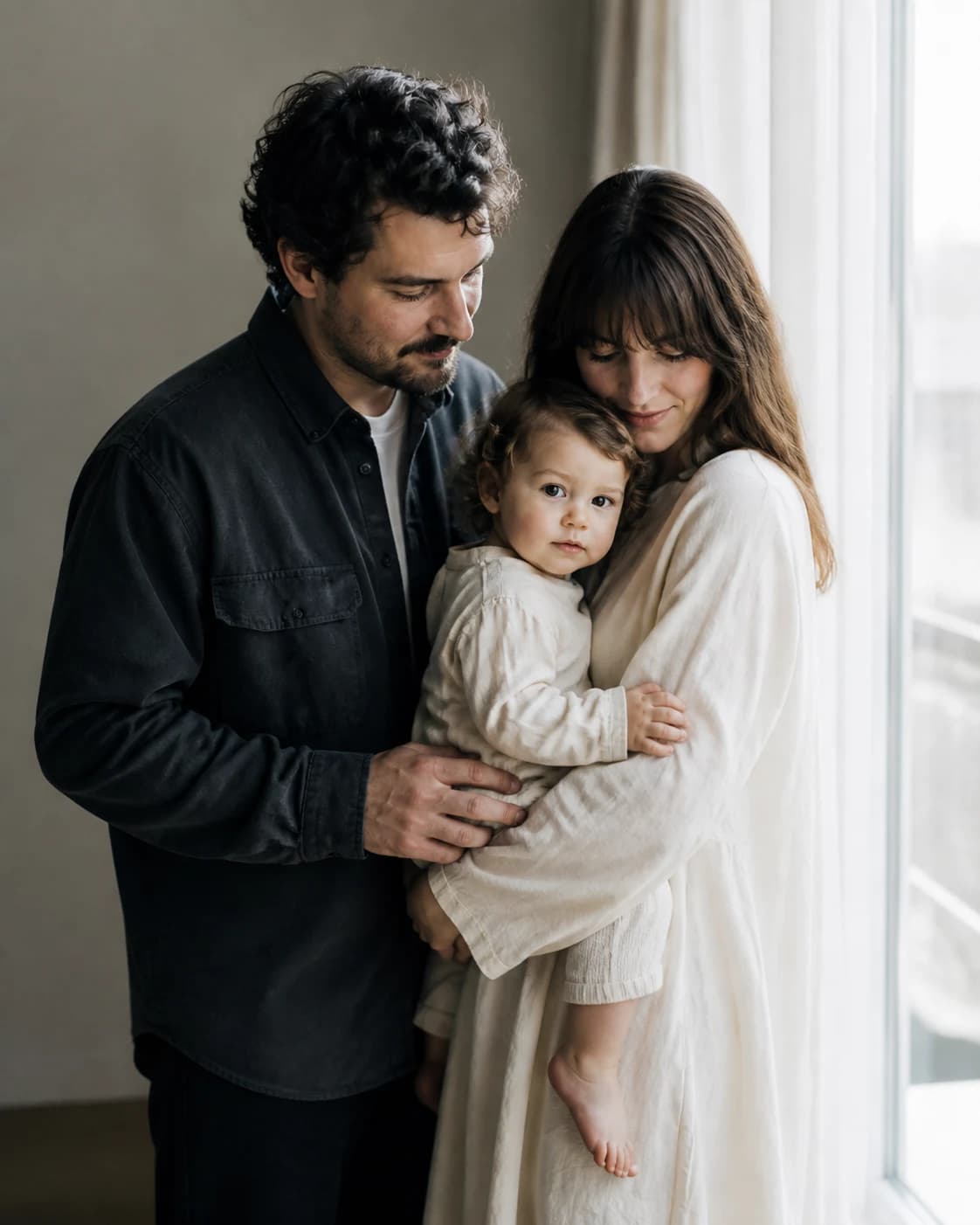 Parents holding their young child beside a window in soft daylight