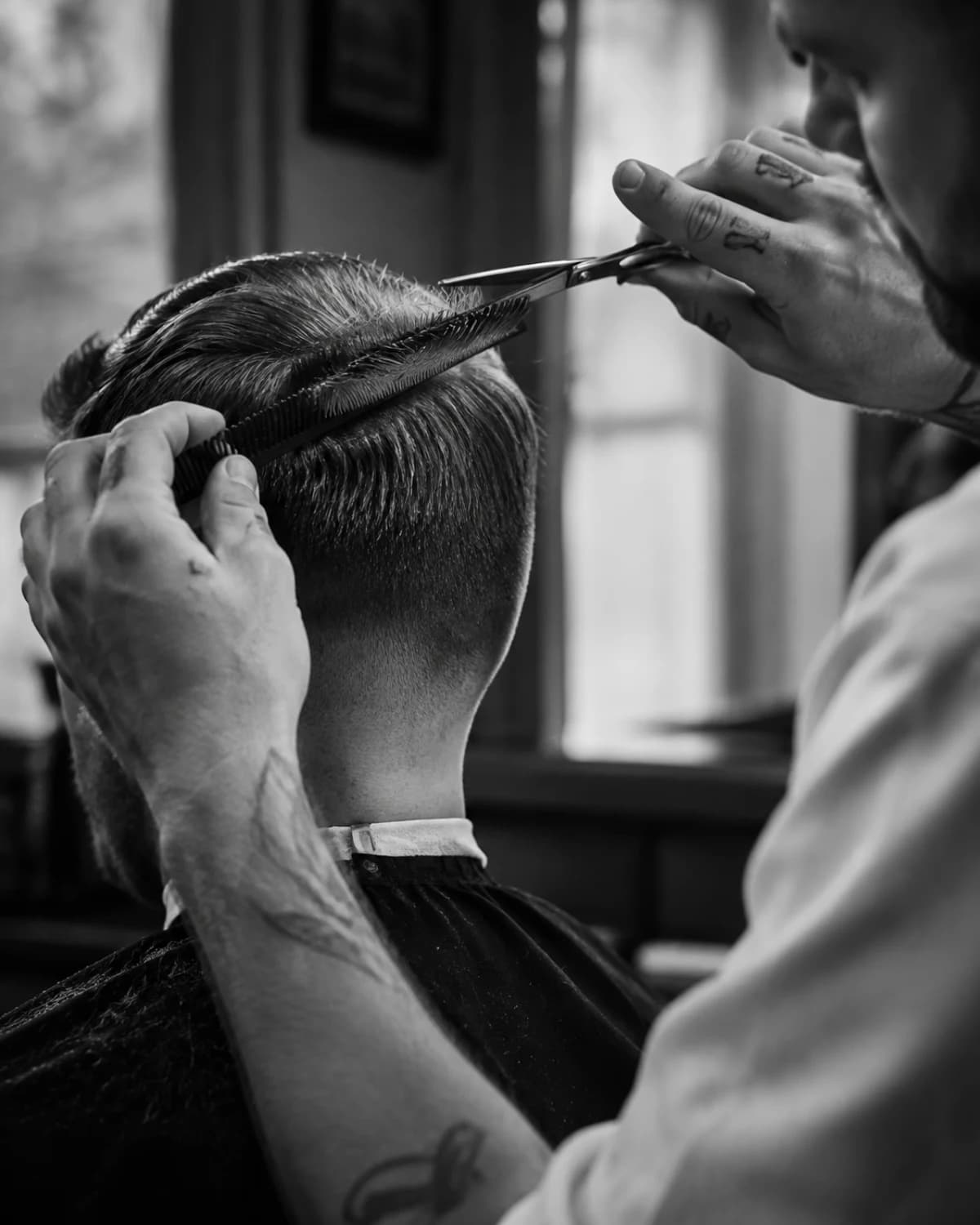 A barber precisely shaping a short haircut with comb and scissors