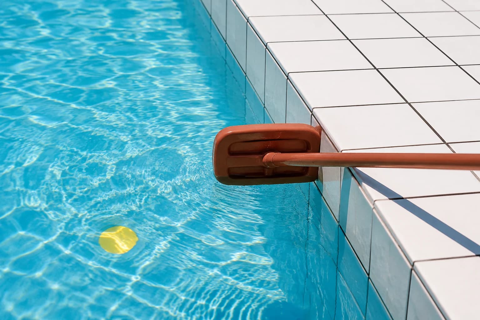 Terracotta pool skimmer crossing clear cyan water beside a white tile edge