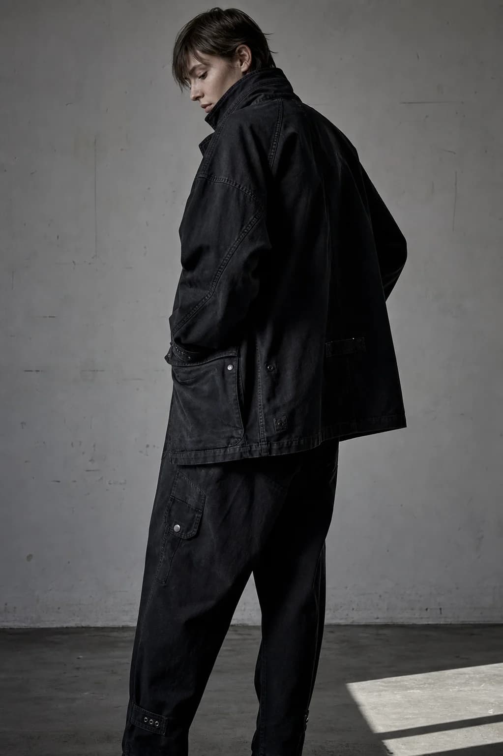 Model in a structured black field jacket photographed against a bare studio wall