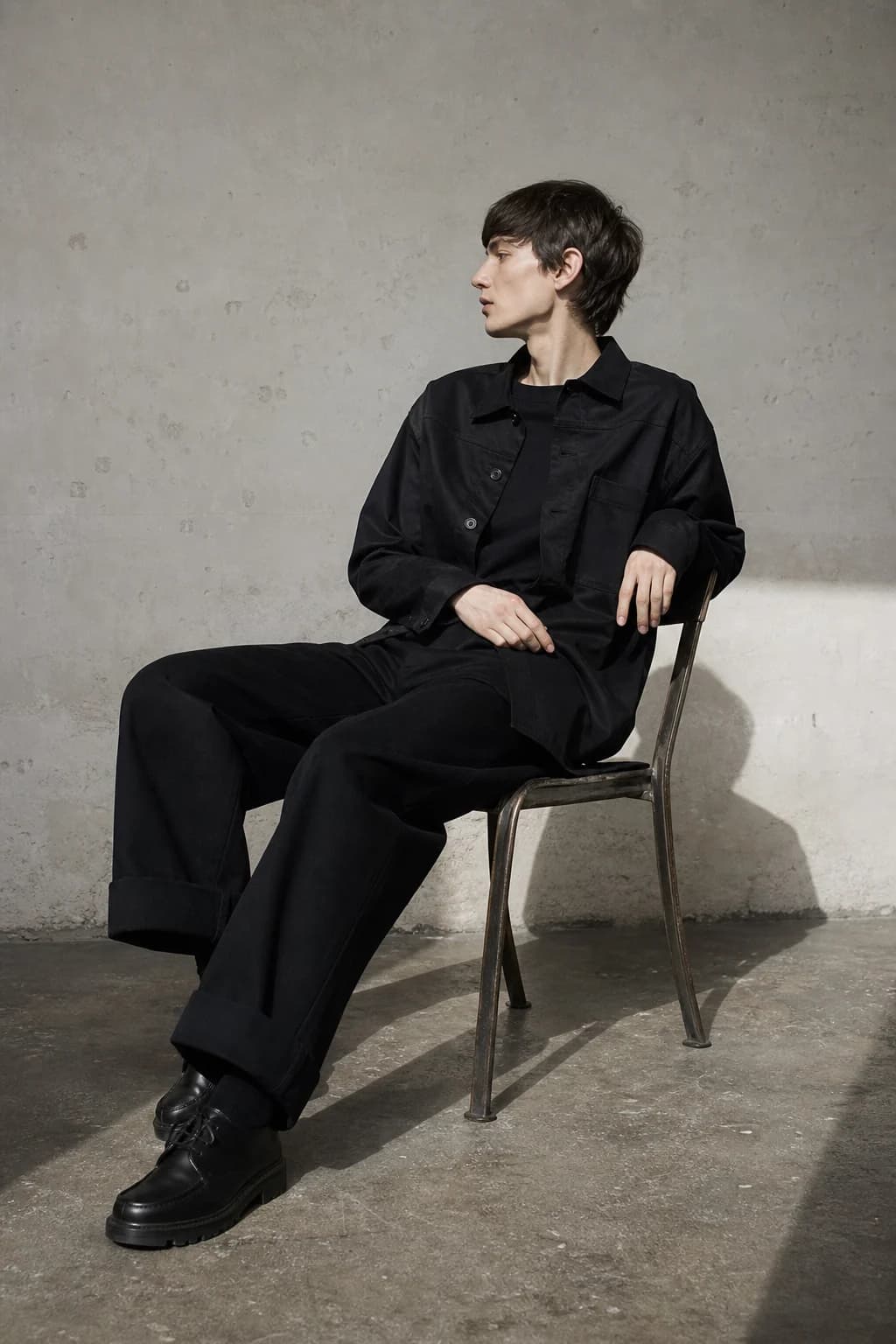 Seated model in a black overshirt and wide trousers