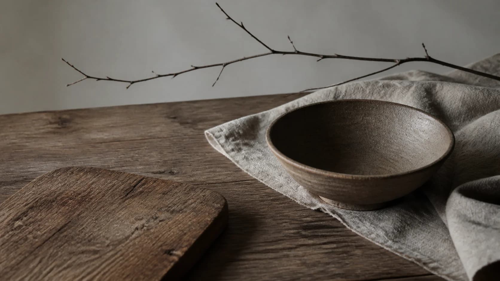 An empty earthenware bowl, linen and a winter branch on a worn preparation table