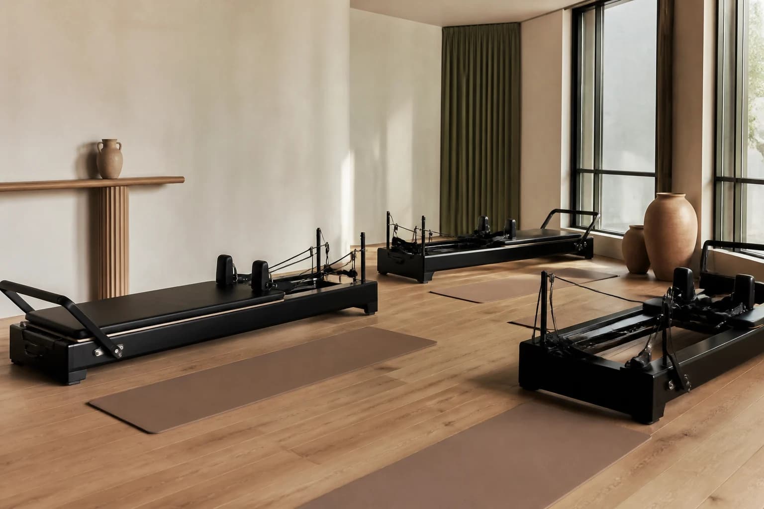 An airy movement studio prepared with black reformers, clay-toned mats, and soft morning light.